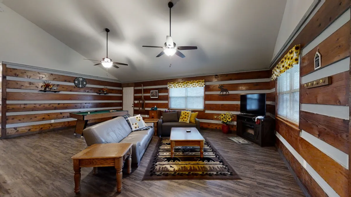 A welcoming living space with wood-paneled walls, a comfortable seating area, a coffee table, and a decorative rug. The open layout suggests easy flow between living and dining spaces, suitable for group interaction and cozy evenings.