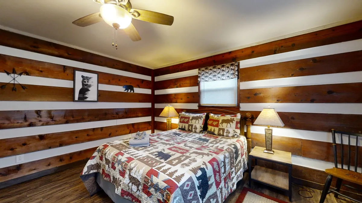 This image features a cozy bedroom with a bed covered in a patterned quilt, wooden walls, table lamps, and rustic artwork. The lighting is warm, creating an inviting and restful atmosphere, ideal for relaxation after a day of adventure.