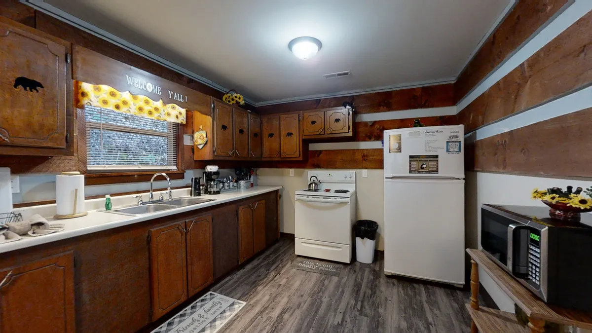 A homey kitchen scene with wooden cabinets, a sink, visible appliances, and a window with patterned curtains. The setup is warm and suggests a space where families can gather to cook, share recipes, and create memories together.