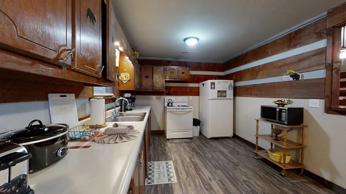 A view of the kitchen area featuring wooden cabinetry, countertop appliances, refrigerator, and warm wooden accents. The space looks well-equipped and ready for family cooking sessions or baking, with plenty of counter space and essential appliances on display.