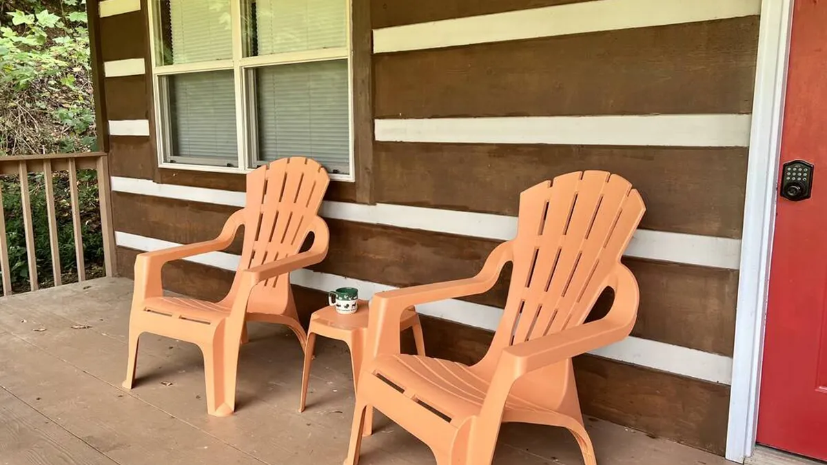 The front porch features vibrant orange chairs facing outwards toward nature, set against a rustic wooden wall and a red door, capturing a serene spot to enjoy morning coffee or unwind while taking in the views.