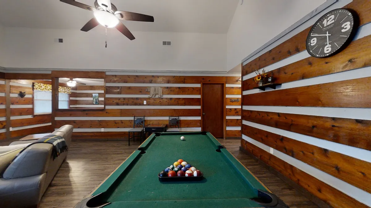 This interior scene features a pool table set against wooden wall paneling, with a clock and a cozy seating area nearby. The space is clearly designed for fun group activities and friendly competition, making it ideal for game nights or social gatherings.